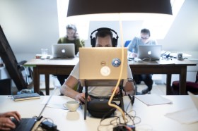 Man sits behind computer, with only eyes and headphones showing