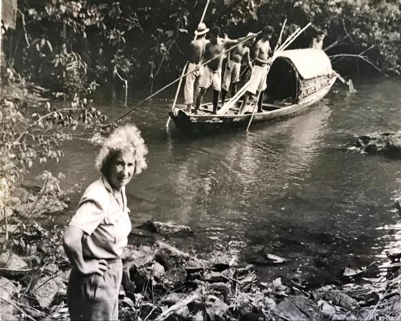 Anita à beira de um rio em frente canoa com índios