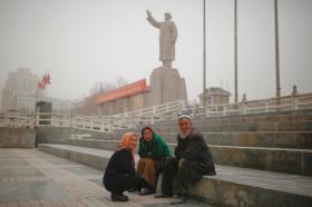 رجل وامرأتان من مسلمي الصين جالسون في ساحة شاسعة وفي الخلفية تمثال ضخم