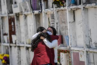 Dos mujeres con mascarillas se abrazan en un panteón