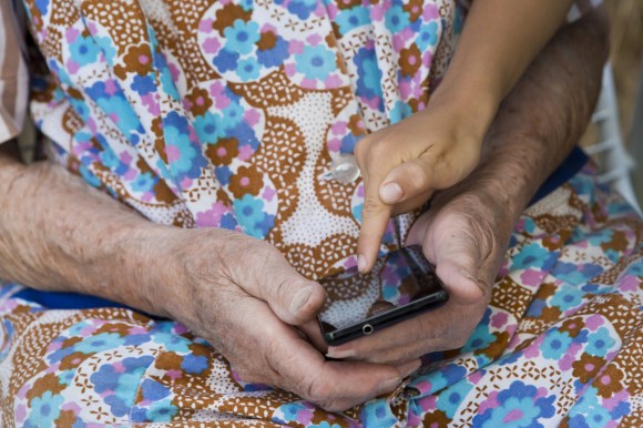 Se aprecian las manos de una persona mayor y una mas joven con un celular