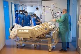 Nurses around a bed in a hospital corridor