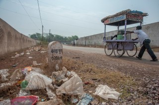 On a littered street in India a man pushes a cart.