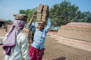 Two women carrying piles of bricks on their heads.