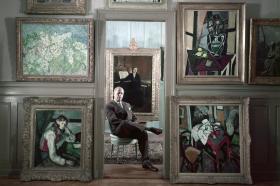رجل يجلس وسط مجموعة من اللوحات والرسوم