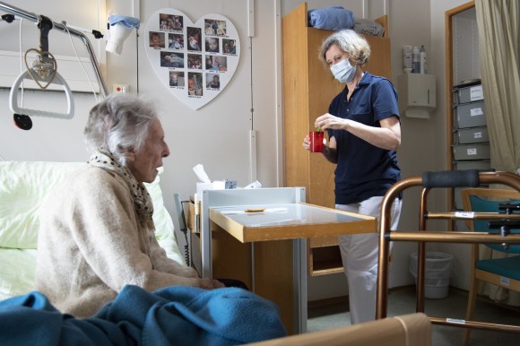 old woman sitting on bed and nurse wearing a face mask