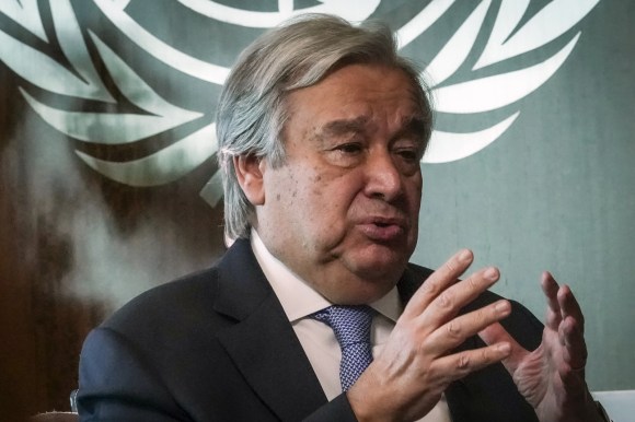 Primo piano di Guterres che spiega qualcosa con un gesto delle mani; sul fondo, effige Onu