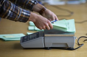 una persona mette delle schede di voto su una bilancia di precisione.