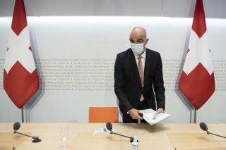 رجل يَستعد لمغادرة مؤتمر صحفي وفي الخلفية أعلام سويسرية
