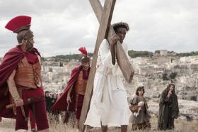 Ator negro como Jesus carregando a cruz e observado por soldado romano