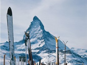 Skis plantés dans la neige avec une montagne en arrière-plan.