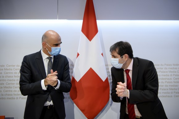 Two men wringing hands beside a Swiss flag