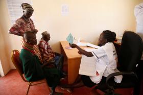 ممرضة كينية تجلس وراء مكتب وأمامها ثلاثة أشخاص
