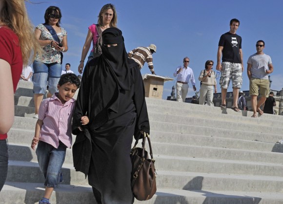 Une femme en niqab marche avec un enfant, descendant des escaliers en ville de Paris