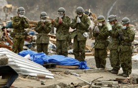 Japanese rescuers pray by a body