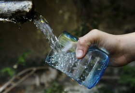 acqua che sgorga da una fontana e una mano che la raccoglie con un bicchiere