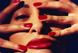 أصابع وشفاه امرأة مطلية باللون الأحمر الفاقع