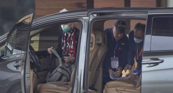 ثلاثة أشخاص يرتدون أقنعة صحية يتحادثون أمام باب سيارة مفتوحة