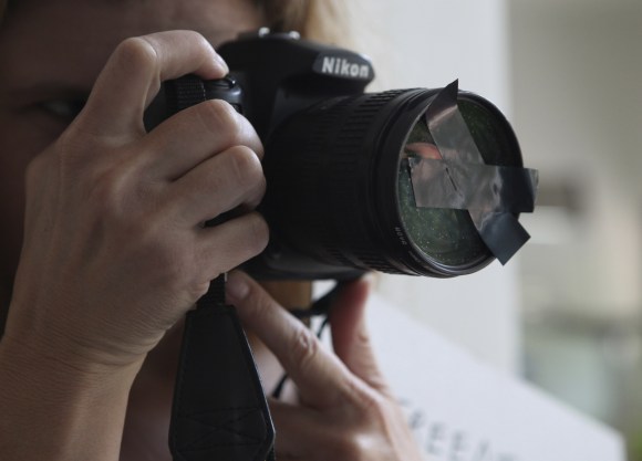 Una persona apunta con una cámara fotográfica cuyo lente está cubierto con cintas adhesivas en cruz