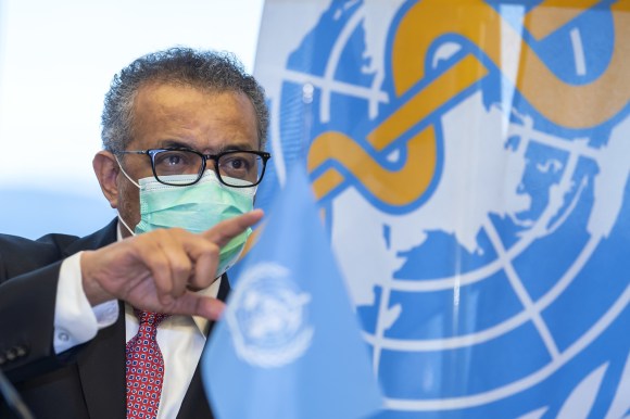رجل يرتدي كمامة وفي الخلفية شعار منظمة الصحة العالمية