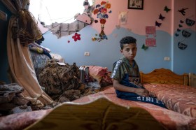 Palestinian boy sitting in his bedroom destroyed by an airstrike
