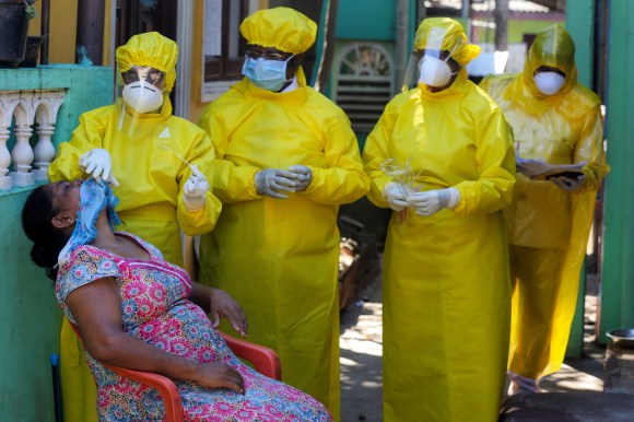 Health workers in yellow protective gear perform swab test on woman