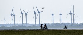 People ride bicycles on a dike at Norderney island, Germany, in front of wind turbines, June 1, 2021.