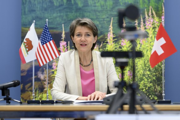 La ministre suisse Simonetta Sommaruga assise à un bureau devant des drapeaux de Suisse, des Etats-Unis et de la Californie.