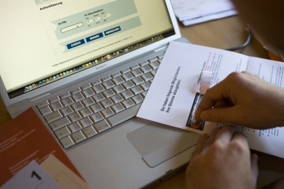 Una persona con un documento de voto, ante una computadora.