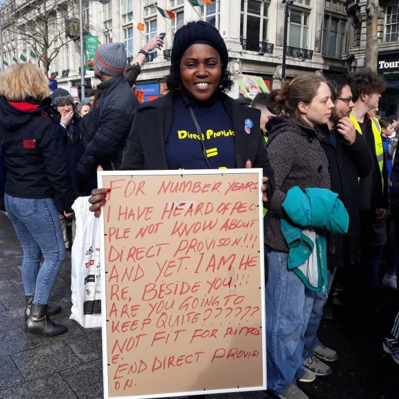Femme noire avec un pancarte dans une rue.