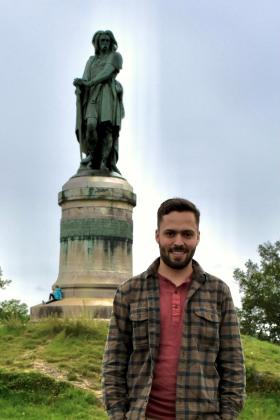 A bearded Lucas Schmid stands by a monument of an ancient warrior