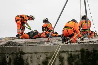 أعضاء فريق سلسلة الإنقاذ السويسرية يستعدون لإنقاذ دمية مصابة من سطح مبنى منهار.