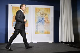 SNB governor Fritz Zurbrügg walks in front of posters of Swiss franc bank notes.