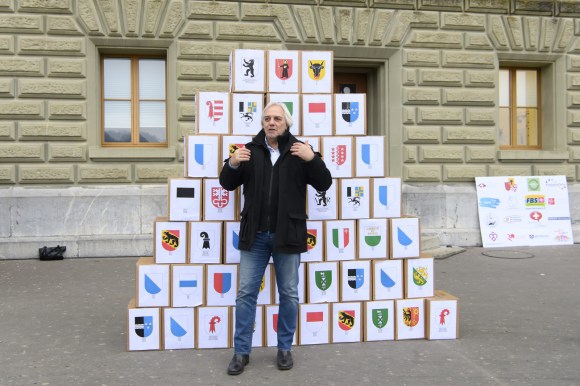 Mans standing in front of pyramid of boxes with cantonal coat of arms