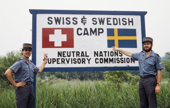 رجلان بزي عسكري يُشيران إلى لافتة مرسوم عليها علما سويسرا والسويد