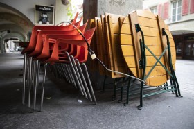 Stacked up plastic chairs and wooden tables outside a restaurant