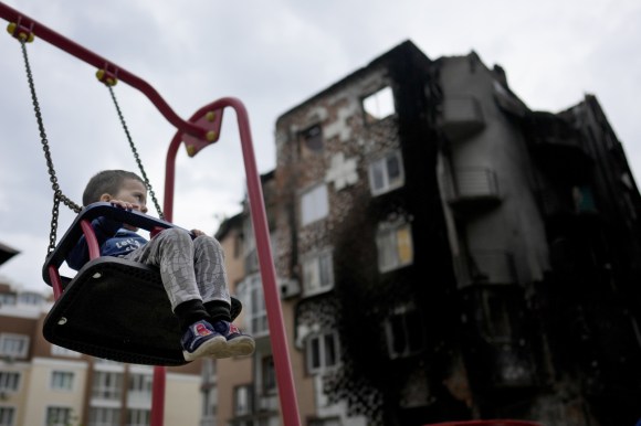 Child plays in front of damaged building.