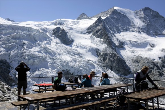 gente che osserva un ghiacciaio da una capanna alpina