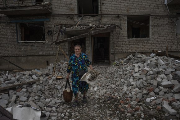 امرأة تحمل أغراضا بسيطة لدى مغادرتها بناية مدمرة في أوكرانيا