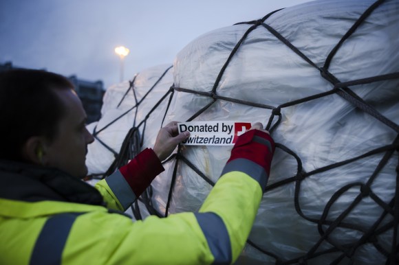 عامل يقوم بتثبيت مُلصقات تحمل عبارة تبرعت بها سويسرا على شحنة إعانات متجهة إلى أوكرانيا
