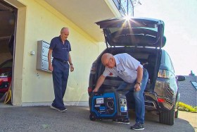 Two men unloading a generator from the trunk of a car