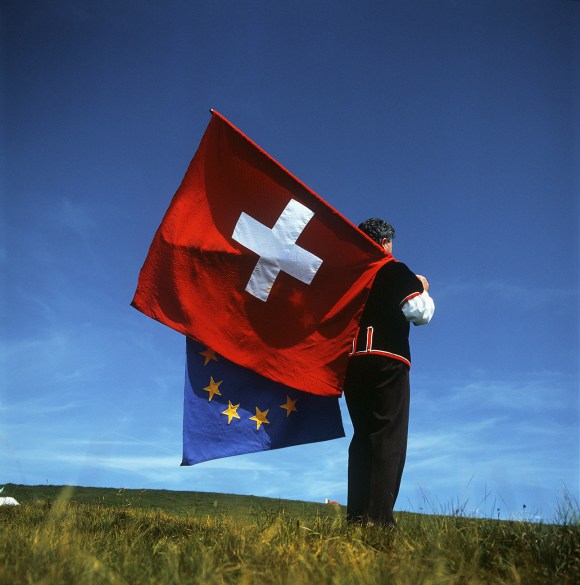 رجل يرتدي لباسا تقليديا ويحمل علمي سويسرا والاتحاد الأوروبي
