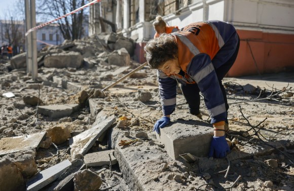 Woman clears rubble in street in Ukraine after a bomb blast