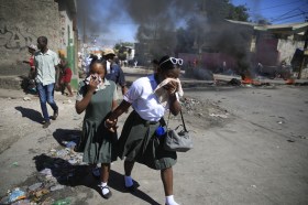 Dos niñas con uniforme de colegio tapándose la nariz y boca por el humo de las protestas en Puerto Príncipe, Haiti