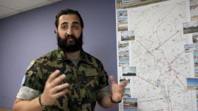 Roman Gagua teaches observers the type of armaments to look for. (swissinfo.ch) Swiss soldier in assault gear in front of a map