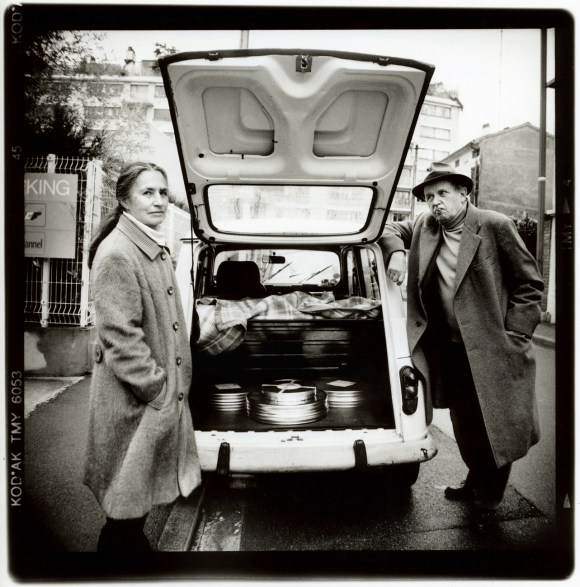 DaniÈlle Huillet und J-M Straub neben einem Auto mit offenem Kofferraum, gefüllt mit Filmdosen