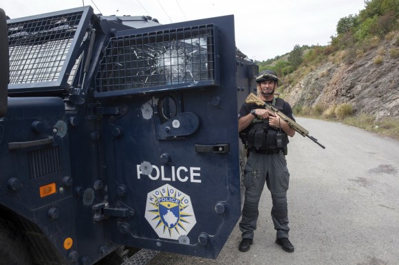 Kosovo, Banjska: Polizist steht neben bewaffnetem Fahrzeug mit Einschusslöchern