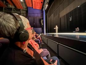 A woman wearing headphones sits in the front row of a theater.