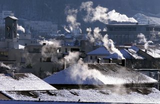 Schneebedeckte Dächer von Häusern, aus deren Schornsteinen Rauch aufsteigt